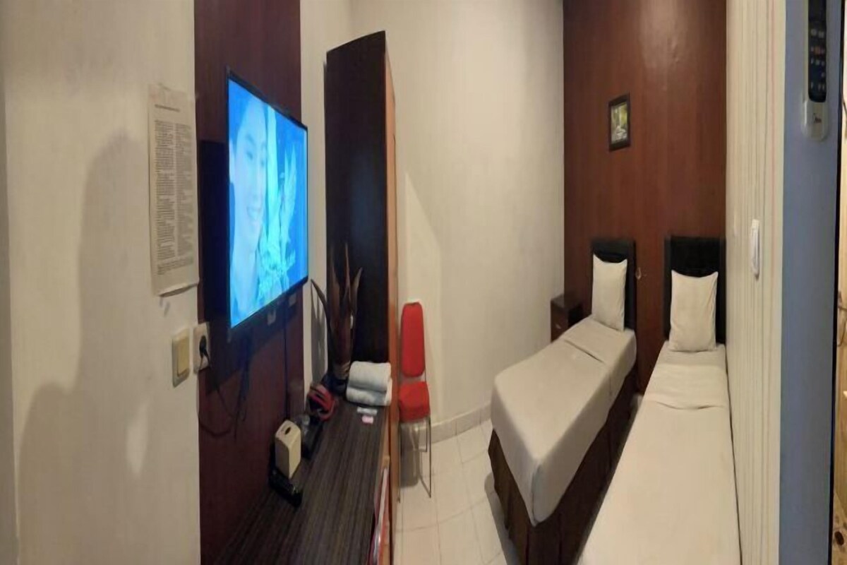 Une chambre d’hôtel avec un lit, une télévision, un fauteuil rouge et une petite table.