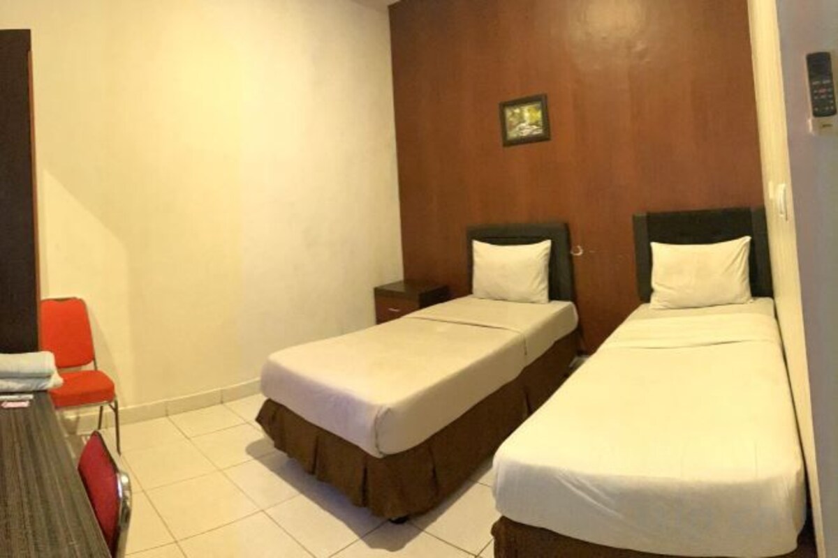 Habitación de hotel con dos camas, una silla roja y una mesita.