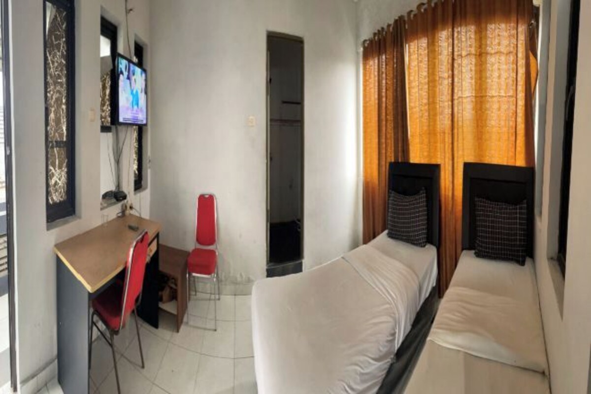 A room with a bed, a desk, a chair, a television, and a window with curtains.