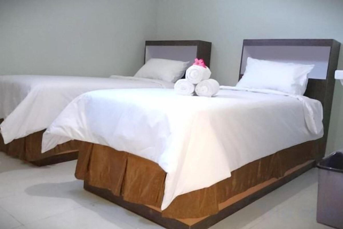 A hotel room with two single beds, each with a wooden headboard, white bedding, and a small bedside table with a lamp.