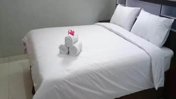 A neatly made bed with white linens and a rolled towel with a pink flower.