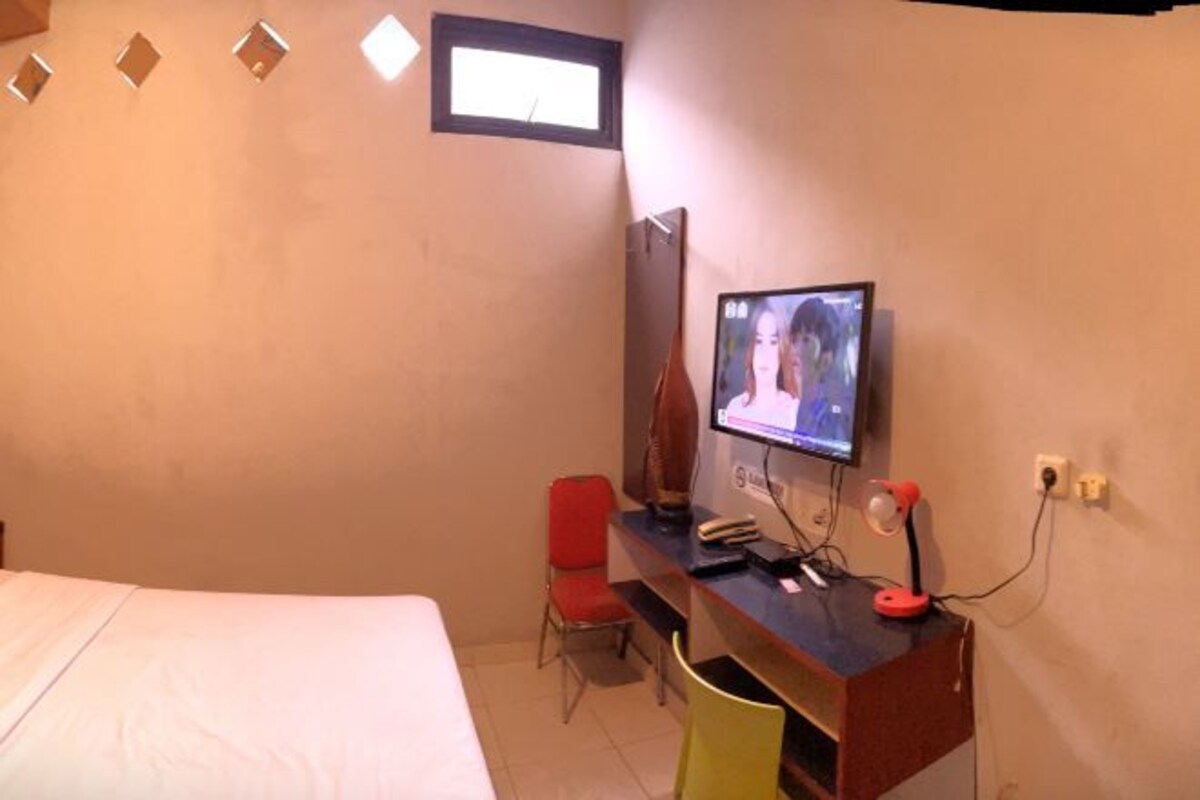 A hotel room with a bed, a desk with a computer, a chair, and a TV on the wall.
