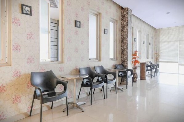 A hotel lobby with a row of black chairs and tables, large windows, and a decorative vase.