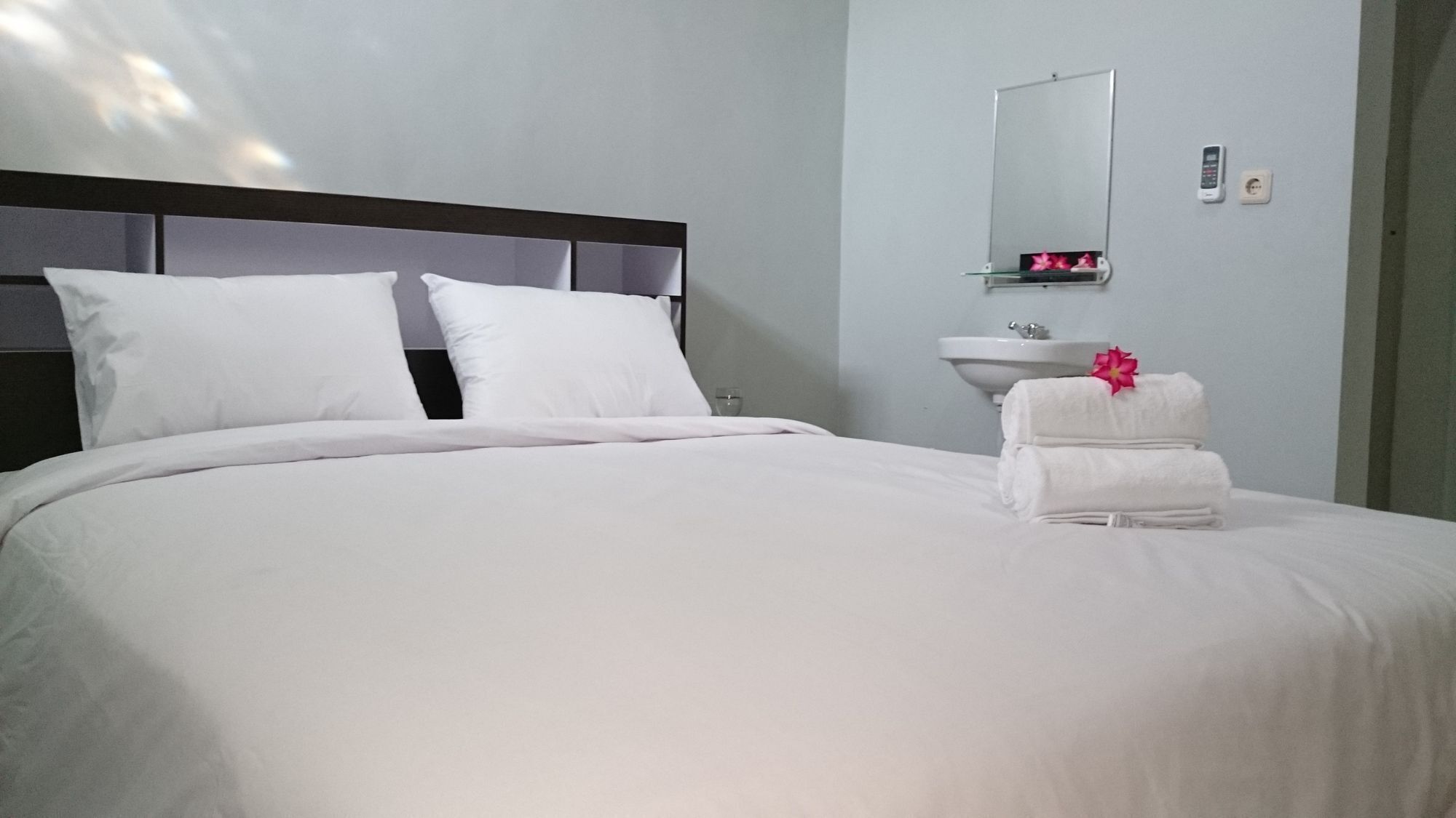 Habitación de hotel con una cama grande, una mesita de noche, un espejo y un lavamanos pequeño.