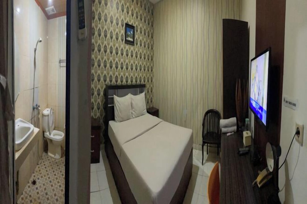 A hotel room with a bed, a television, a desk, a chair, a bathroom with a sink and toilet, and a patterned wall.
