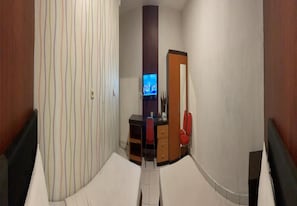 Une chambre d’hôtel étroite, avec un lit, un bureau et un téléviseur.