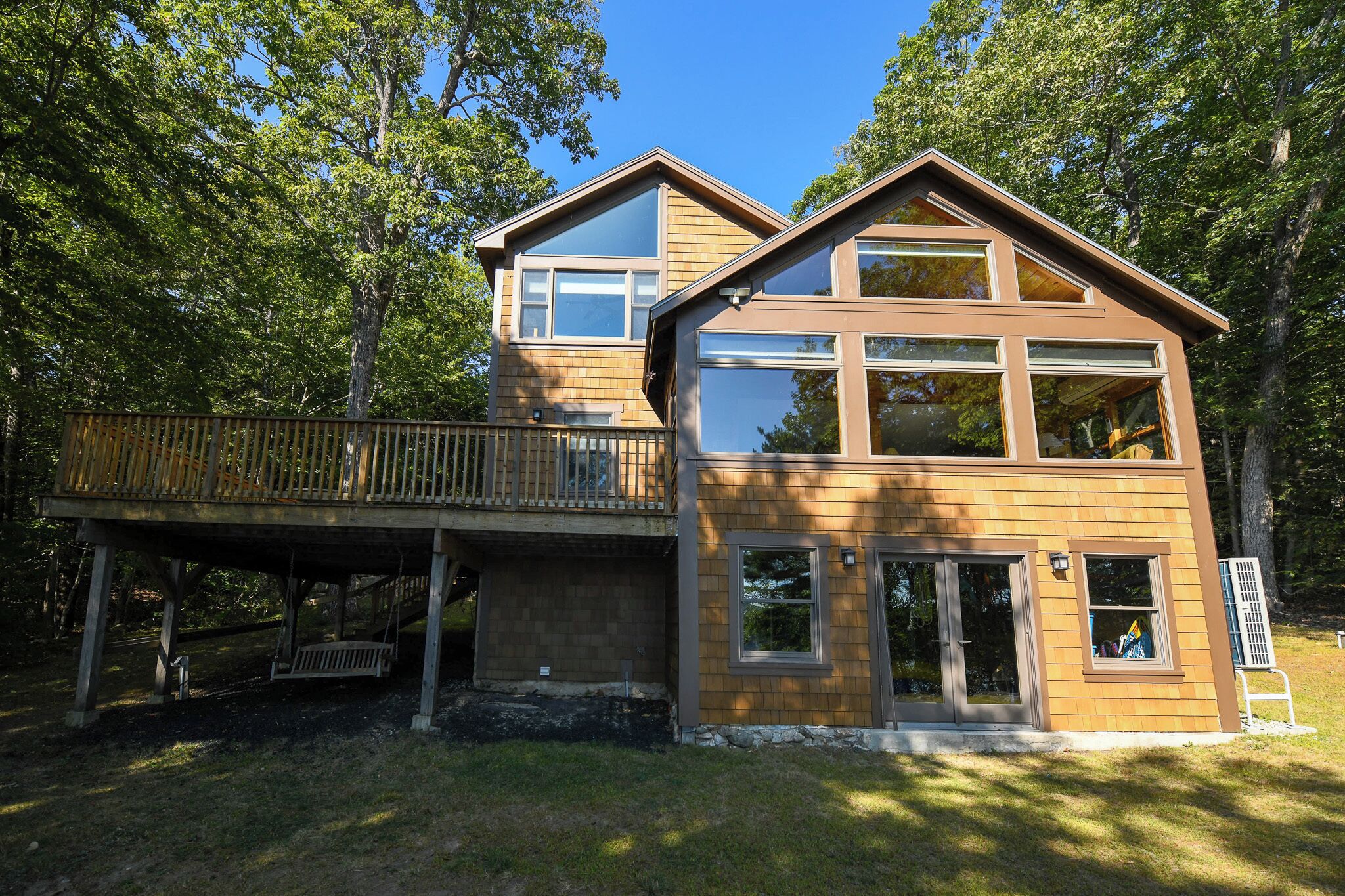 Une maison en bois à deux étages, dotée d’une terrasse, de grandes fenêtres et d’un garage.