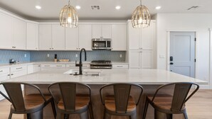 Une cuisine moderne avec des armoires blanches, un grand îlot central doté de tabourets, un four à micro-ondes et des luminaires suspendus.