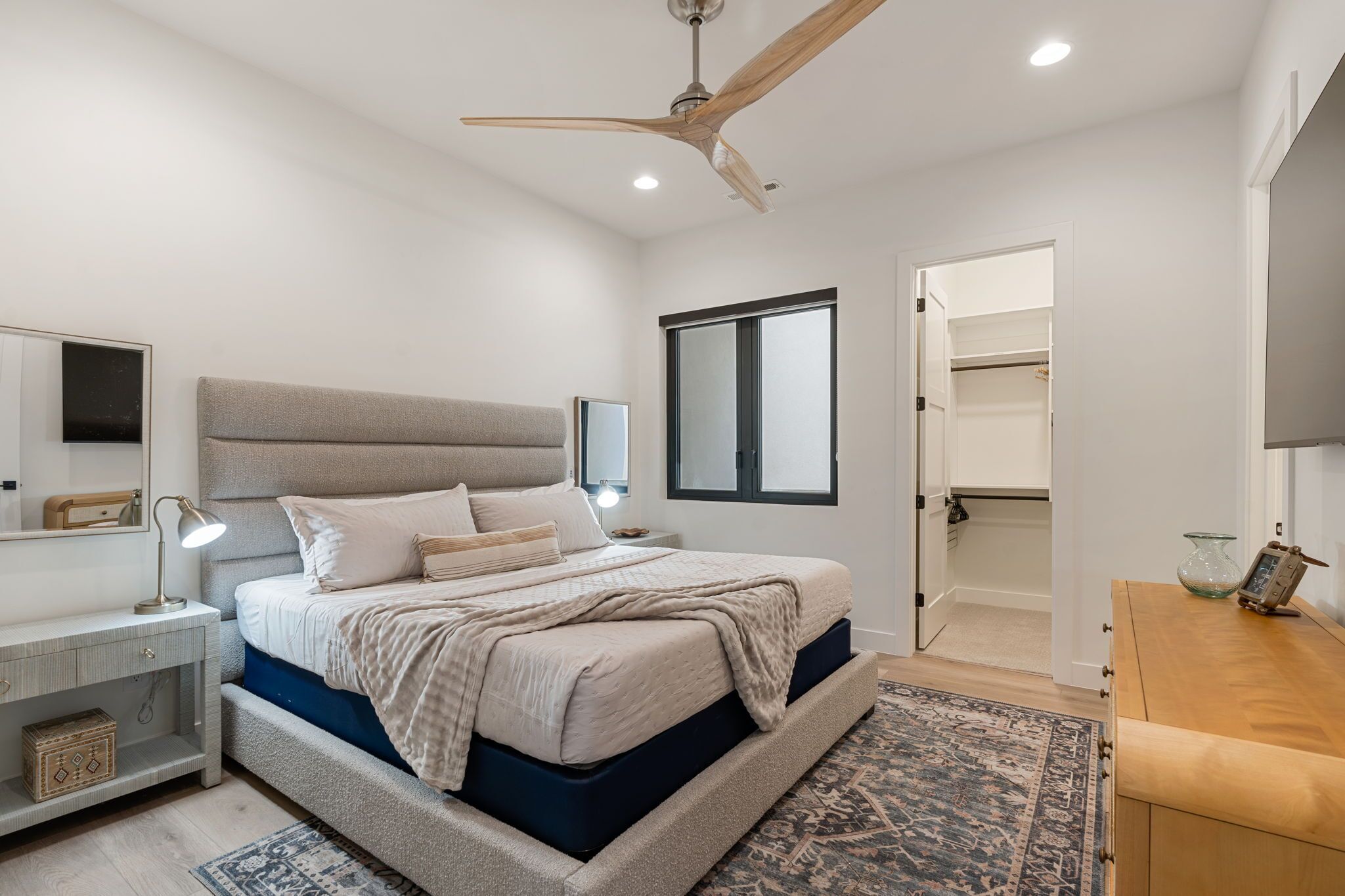 Une chambre à coucher comprenant un lit, une table de chevet, une lampe, un ventilateur de plafond et donnant sur un placard.