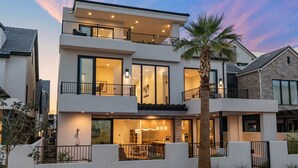 A modern two-story house with a balcony, large windows, and a well-lit interior. - Lula Bay Lagoon House: Private Pool + Near Lagoon (St. George)