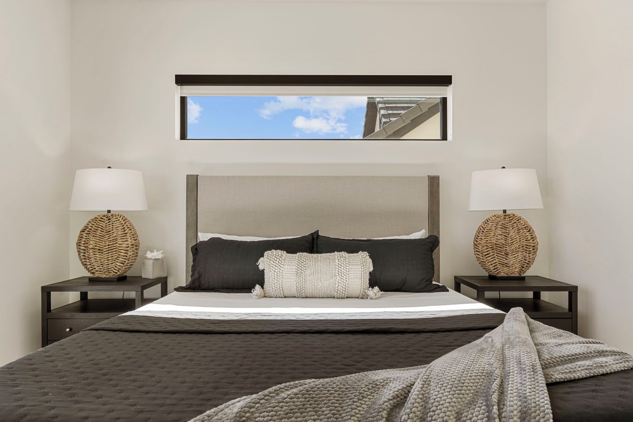 A modern bedroom with a large bed, two bedside tables with lamps, a headboard, and a view of a building through a window.