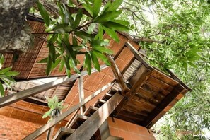 A wooden staircase leading to a brick building with a bamboo tree in the foreground.