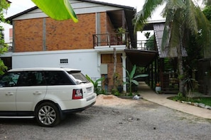 A white SUV parked in front of a two-story building with a brick facade and a covered porch. - ANGKOR DINO HOME (Siem Reap)