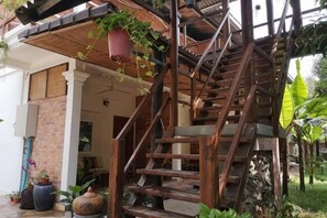 Eine Holztreppe führt zu einem überdachten Bereich mit Blumentöpfen und einer Backsteinmauer.