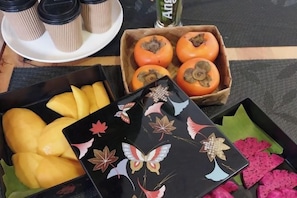 A table with a tray of yellow fruits, a box of tomatoes, and a black tray with decorative patterns. - ANGKOR DINO HOME (Siem Reap)