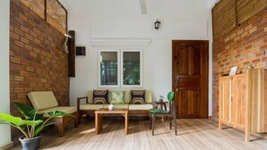 A room with a brick wall, a wooden door, a sofa with cushions, a table, and a chair. - ANGKOR DINO HOME (Siem Reap)