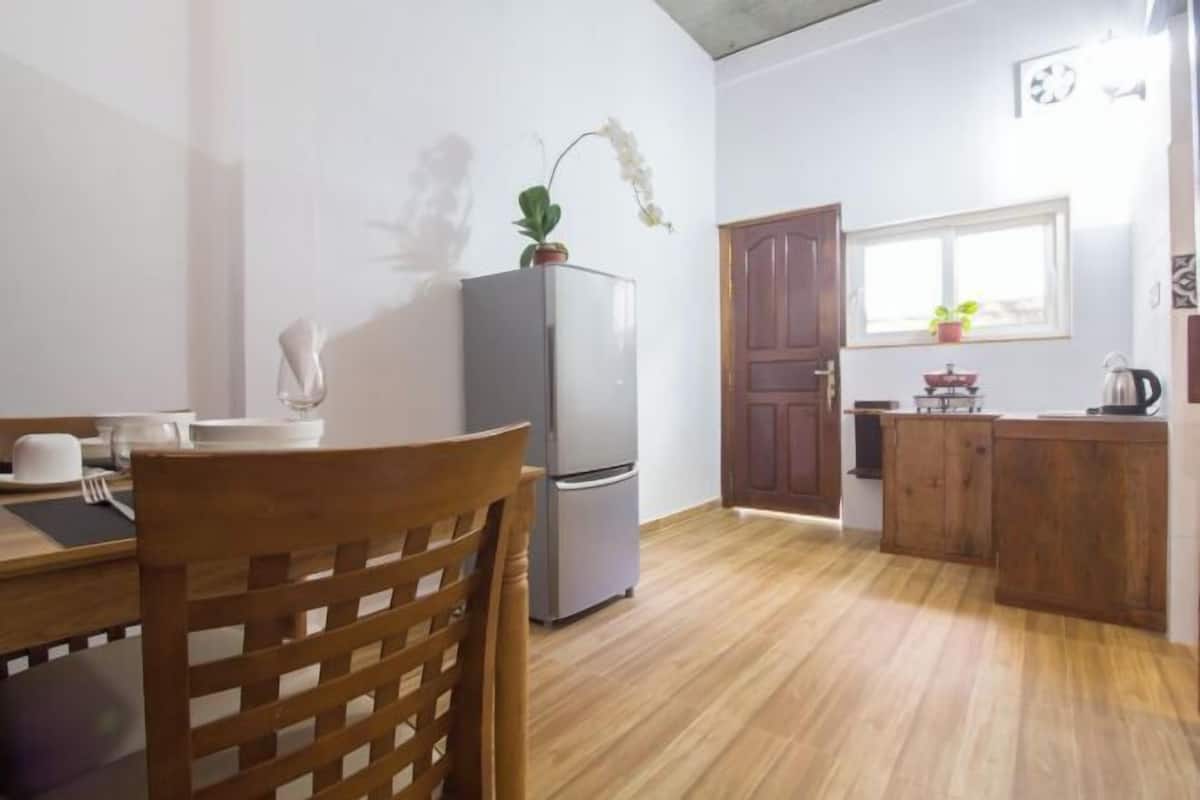 A compact kitchen with a wooden dining table, a refrigerator, and a window with a view.