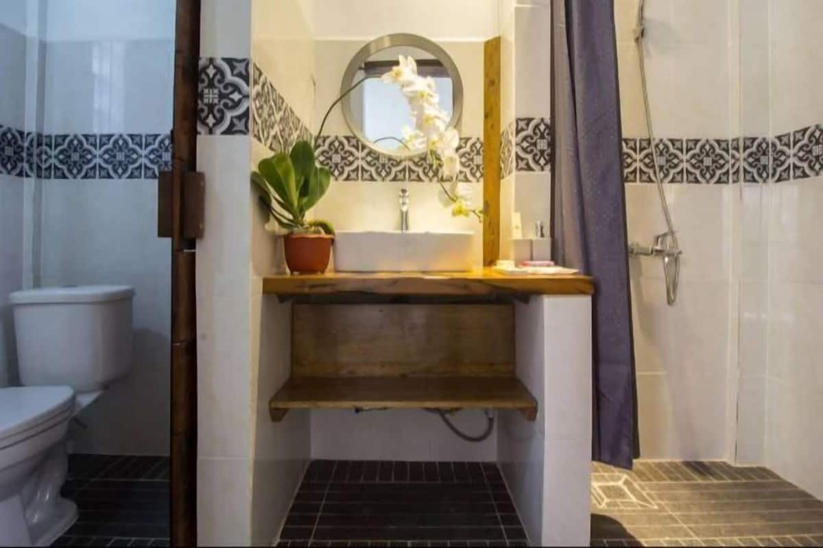 A bathroom with a white toilet, a sink with a mirror above it, a potted plant, and a shower area with a curtain.