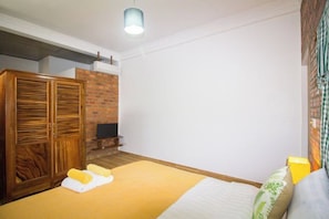 A bedroom with a bed, wooden wardrobe, and a brick wall. - ANGKOR DINO HOME (Siem Reap)