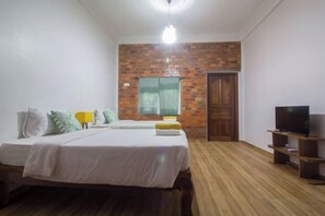 A bedroom with a brick accent wall, a bed, a TV, and a wooden floor. - ANGKOR DINO HOME (Siem Reap)