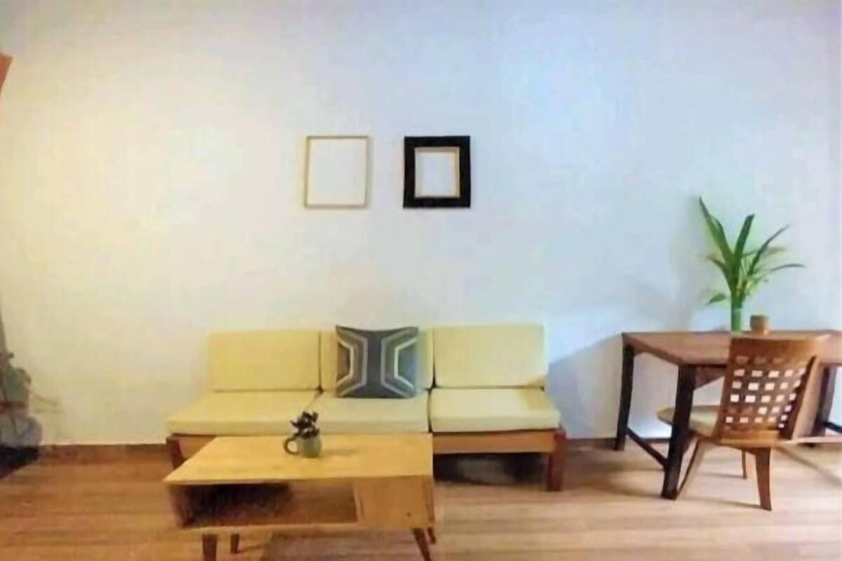 A living room with a sofa, a coffee table, a dining table with chairs, and two framed pictures on the wall.