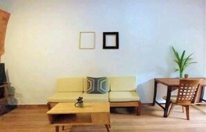 A living room with a sofa, a coffee table, a dining table with chairs, and two framed pictures on the wall.