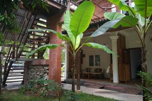 A covered outdoor area with a stone wall, a wooden staircase, and a seating area with a table and chairs. - ANGKOR DINO HOME (Siem Reap)