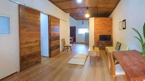 A spacious room with a wooden floor, a dining table with chairs, a sofa, and a television. - ANGKOR DINO HOME (Siem Reap)