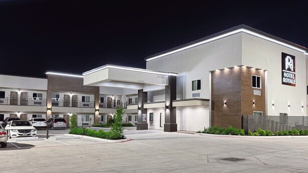A modern hotel with a prominent sign, multiple floors, and a parking area with several cars. - Hotel Royale (Houston)