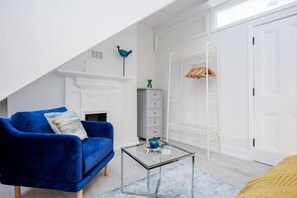 Una habitación con un sofá azul, una mesa de centro de vidrio, un armario blanco y un radiador blanco.