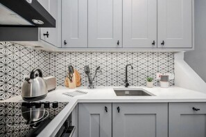 Una cocina con armarios blancos, un salpicadero estampado, una estufa, un fregadero y diversos utensilios.