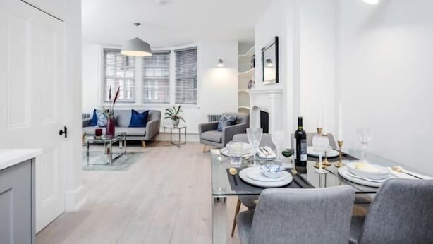 A modern dining area with a glass table set for a meal, a sofa in the background, and a fireplace. - Kula London - Covent Garden St Martin's Lane (London)