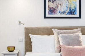 Un dormitorio ordenado con cama, almohadas, una mesita de noche con un cuenco y un interruptor de luz en la pared.