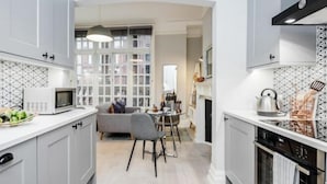 A modern kitchen with white cabinets, a microwave, and a dining area with a gray sofa and table. - Kula London - Covent Garden St Martin's Lane (London)