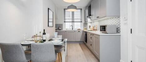 Una cocina moderna con armarios grises, una mesa de comedor con sillas e iluminación colgante.