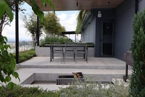 An outdoor patio with a table and chairs, a small dog, and a view of the city. - Pause Apartment (Dalat)