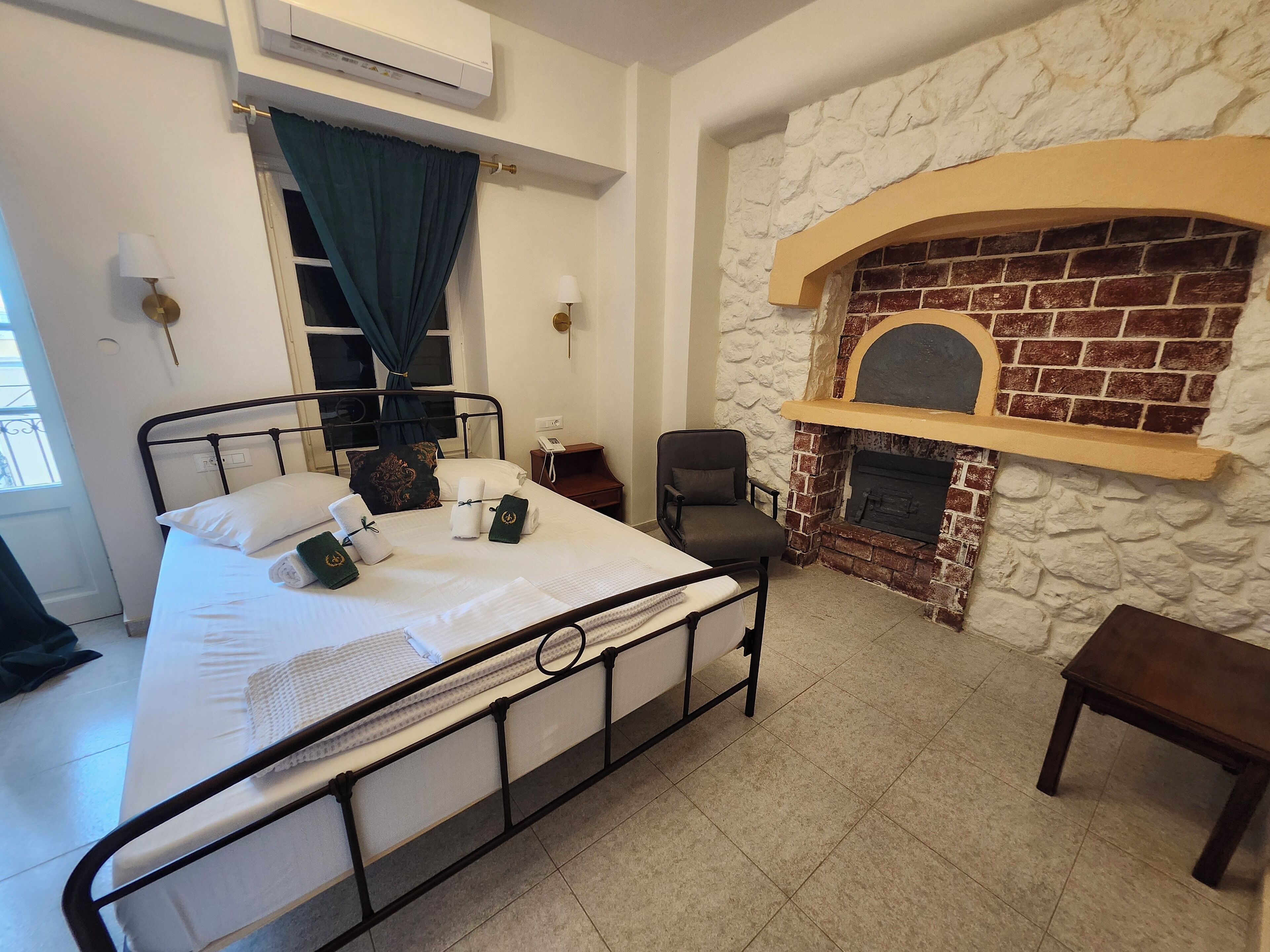 A bedroom with a bed, a chair, a small table, a fireplace, and an air conditioning unit.