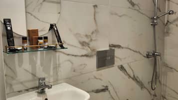 Baño con lavamanos blanco, inodoro, ducha y espejo con aplique dorado.