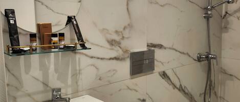 A bathroom with a white sink, a toilet, a shower, and a mirror with a gold light fixture.