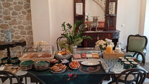 A dining table set with various food items, plates, and glassware, surrounded by chairs and a mirror. - Archontiko Hotel (Kalymnos)
