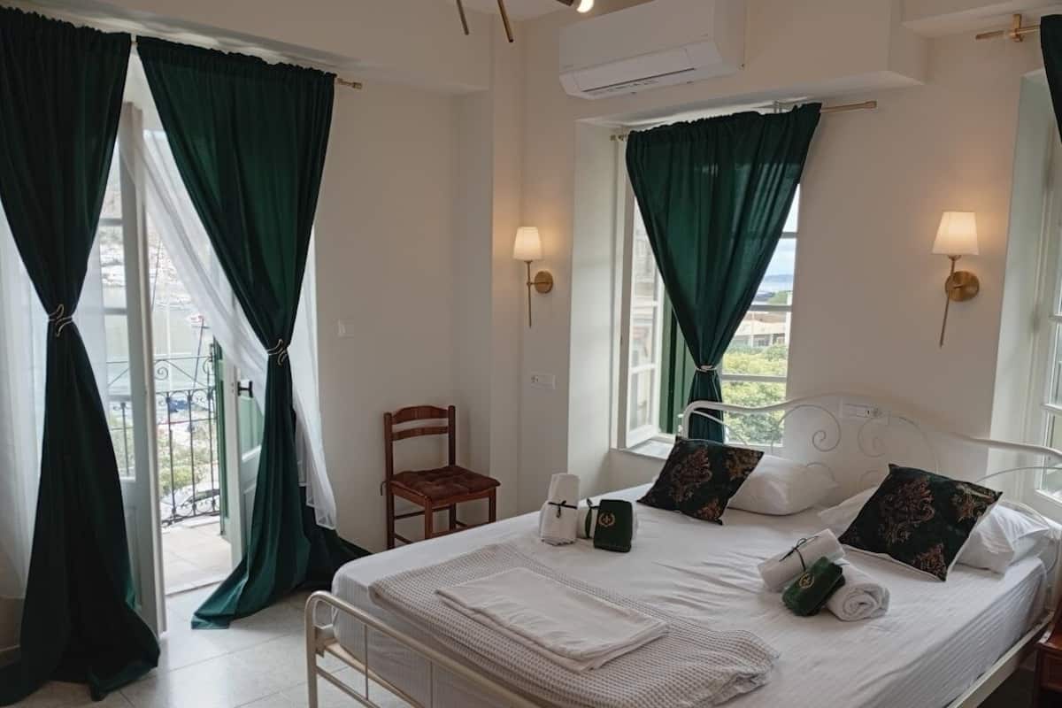 Una cama bien hecha con almohadas y una colcha, una silla, una mesita de noche con una lámpara y una ventana con cortinas.