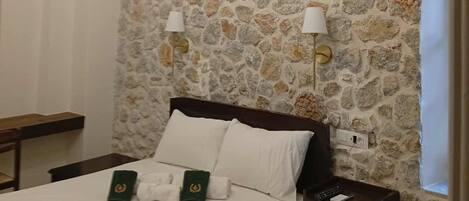 A bedroom with a stone wall, a bed with white linens, two bedside lamps, and a modern chandelier.