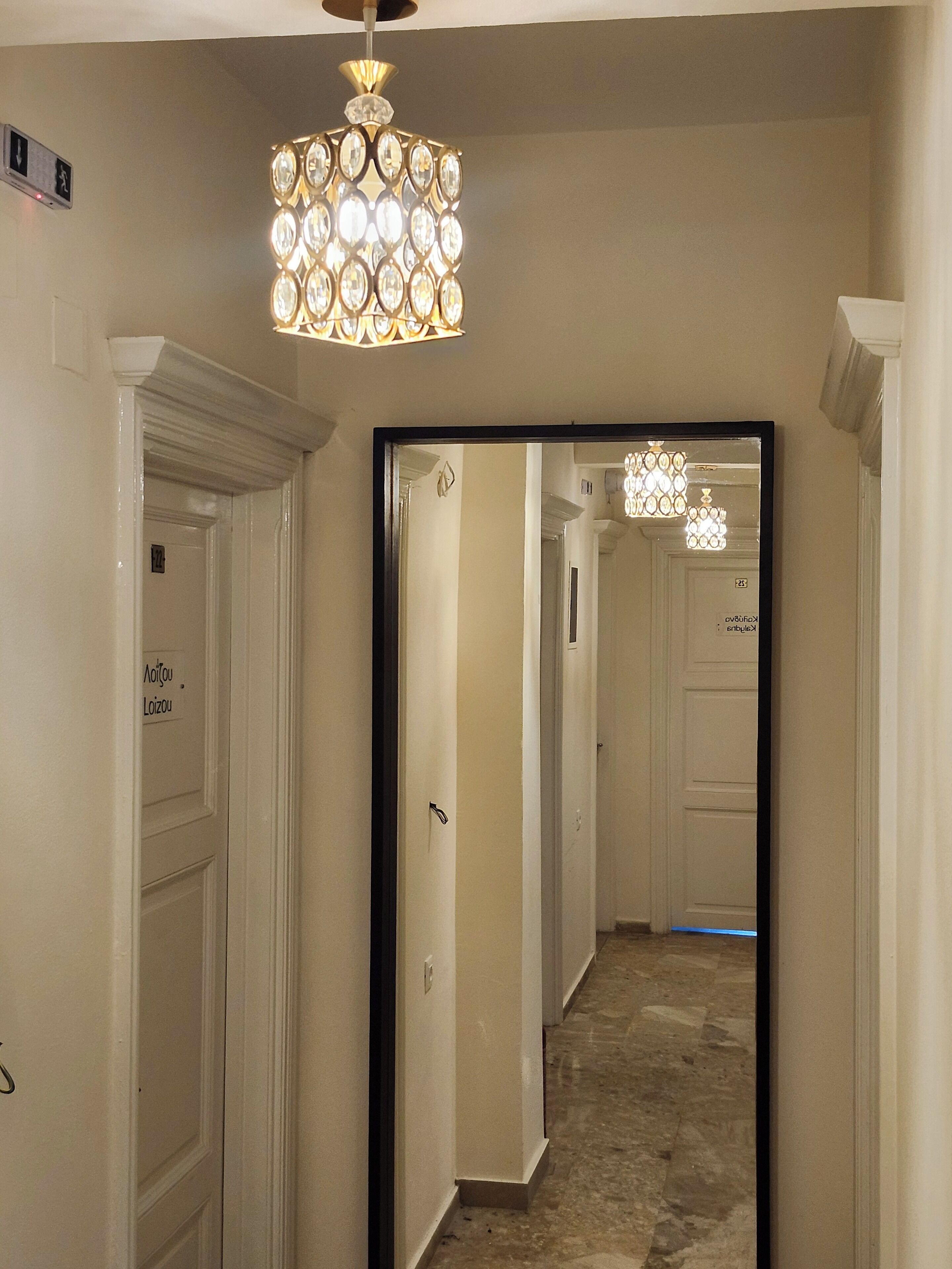 A hallway with a mirrored wall, a chandelier, and a door with a sign.