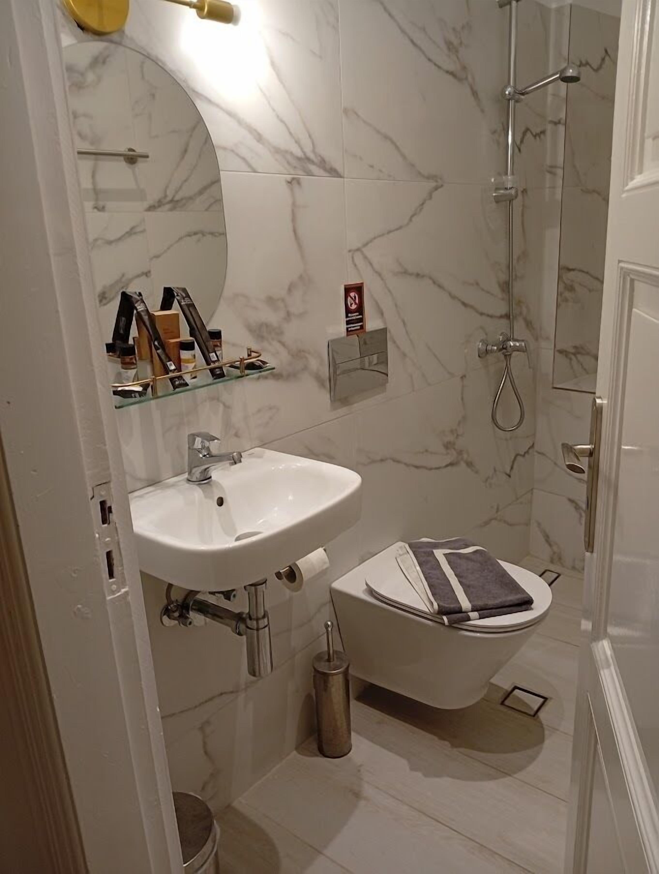 A bathroom with a white sink, a toilet, a shower, and a marble-tiled wall.
