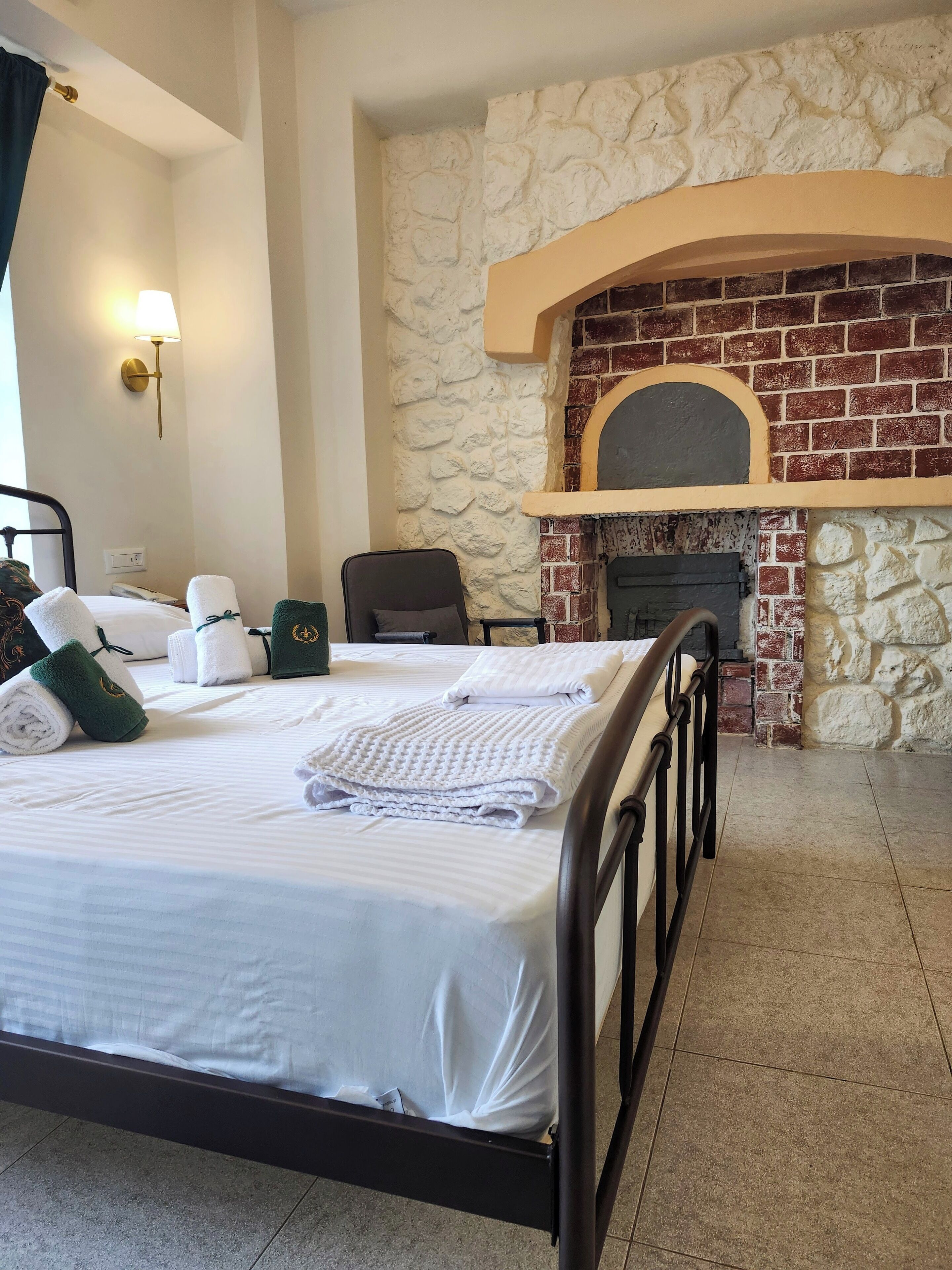 A hotel room with a bed, a stone wall, a fireplace, and a lamp.