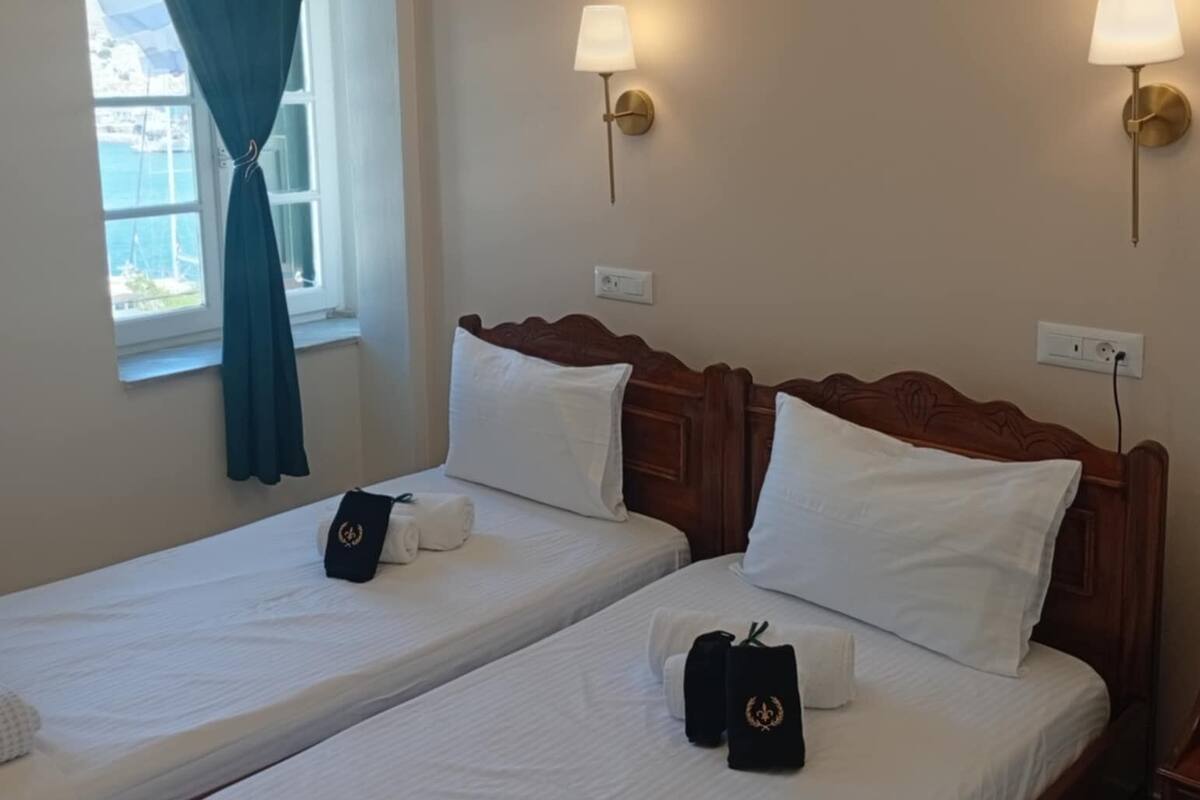 Una habitación de hotel con dos camas individuales, una ventana con cortinas y lámparas fijadas a la pared.
