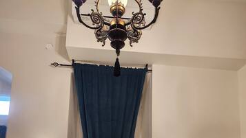 Habitación de hotel con cama, candelabro, dos lámparas de pared y una ventana con cortinas.