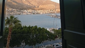 A view from a window overlooking a coastal town with a body of water, boats, and a mountainous backdrop. - Archontiko Hotel (Kalymnos)