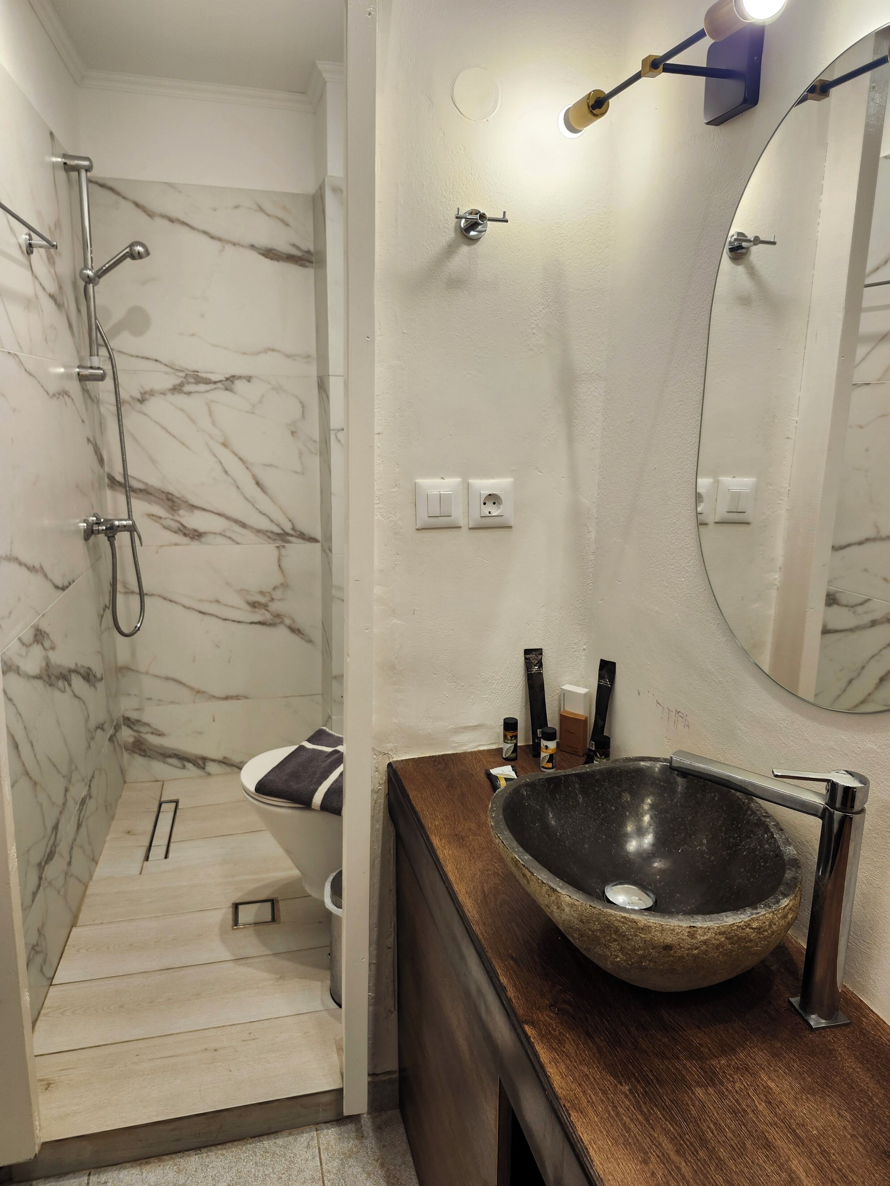 A bathroom with a marble shower, a sink with a stone basin, and a wooden vanity.