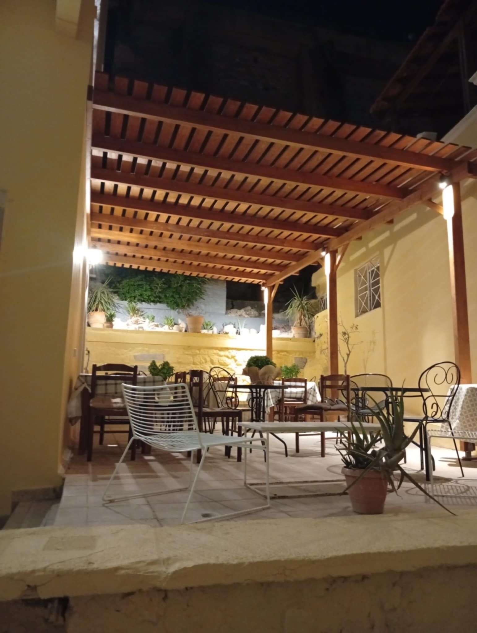 Un espace extérieur aménagé en terrasse, avec une pergola en bois, des tables, des chaises et des plantes en pot.